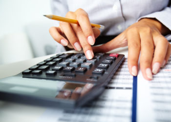 Photo of hands holding pencil and pressing calculator buttons over documents