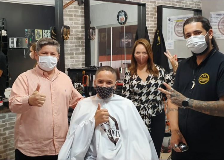 O presidente da APAE, Vander Lúcio Barbosa e a diretora da escola Maria Montessori, Nelma Granja, acompanhando o corte de um aluno pelo barbeiro Wilson Ramos.