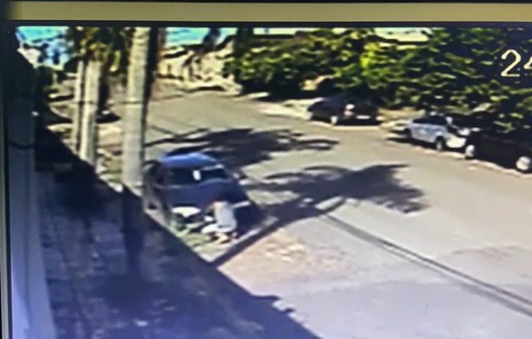 imagem de câmera mostra homem agachado frente a um carro, que teve a bateria furtada
