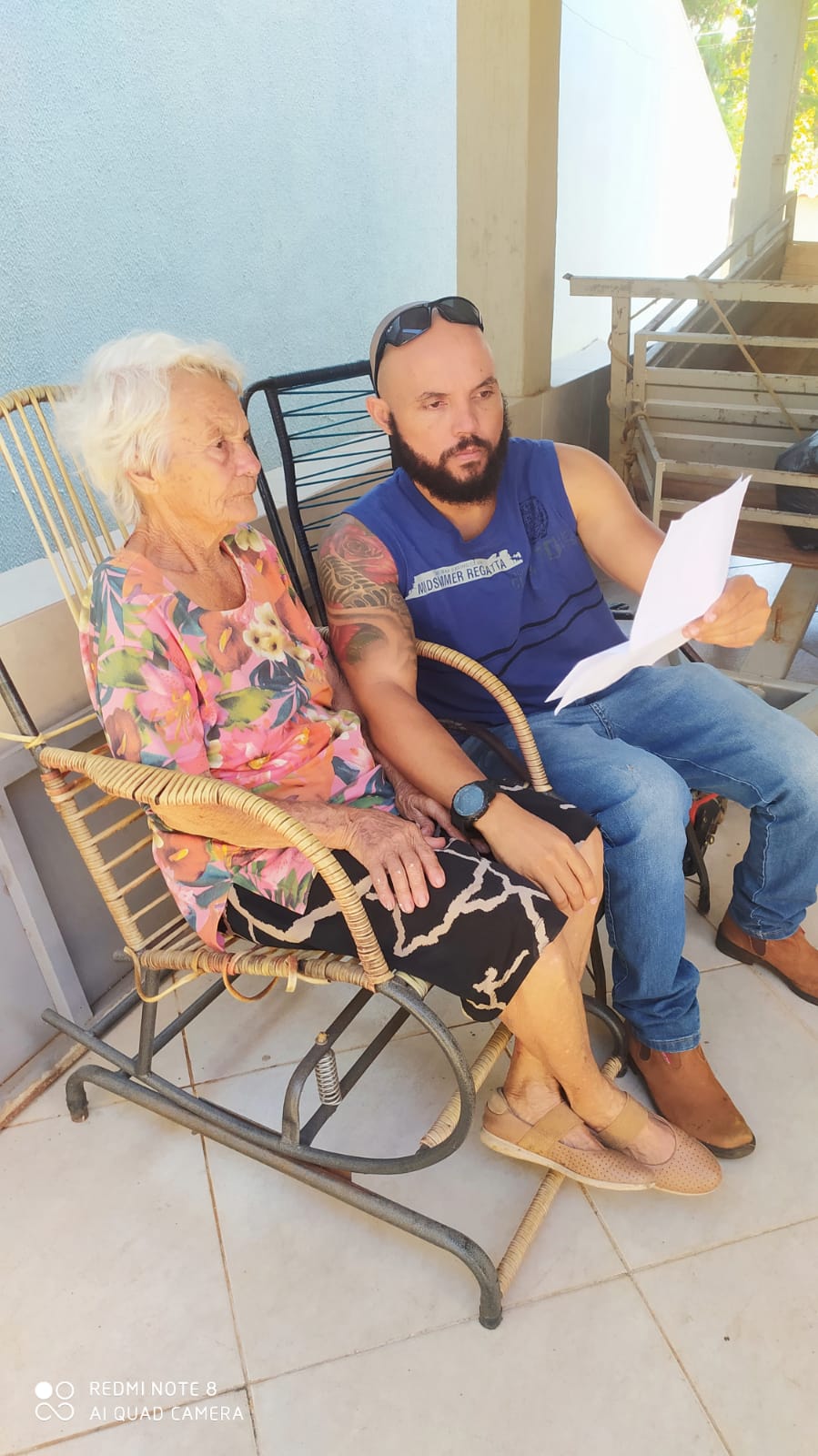 senhora, mae de Laír, sentada ao lado de seu outro filho, ambos estão lendo um papel