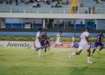 jogador do Grêmio Anápolis carrega a bola pelo campo, ele é seguido por marcadores de azul e acompanhado por companheiros de time