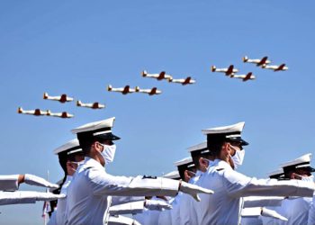 A imagem mostra militares em formação e aviões no céu azul