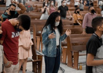 foto de um dos principais e mais tradicionais eventos religiosos de Anápolis: o COMEPE (Congresso das Mocidades Evangélicas Pentecostais). Nela, uma moça ao centro está com as mãos erguidas e orando.