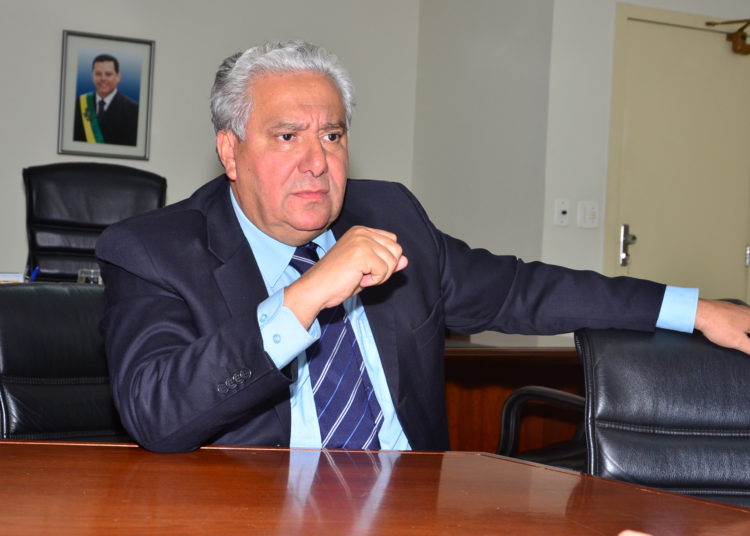 ex-deputado vilmar rocha, sentado e apoiado em mesa, ele veste terno