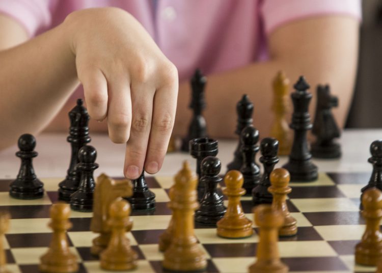 mão mexendo peça em tabuleiro de xadrez