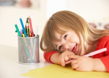 foto de criança portadora da síndrome de down sorrindo ao lado de um pote com lápis e canetas