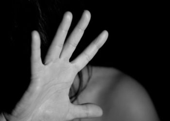 foto retratando violência contra a mulher, em foto acinzentada com mão tampando rosto