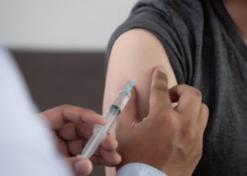 Agente de saúde vacinando braço de um jovem