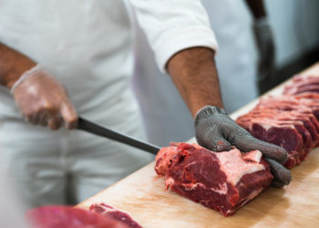 foto retratando o trabalho de açougueiro, com homem de branco e luva cortando carne