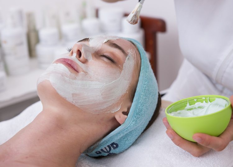 foto de pessoa com o rosto cheio de creme, com mãos de esteticista realizando trabalho ao redor