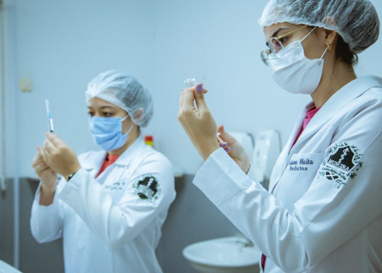 foto de vacinação, com duas enfermeiras segurando vacinas