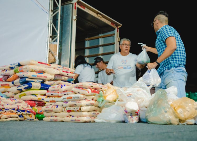 foto da primeira etapa das doações de alimentos arrecadados na expoana. Na foto, um homem passa cesta básica para outro. Ao fundo, um caminhão.