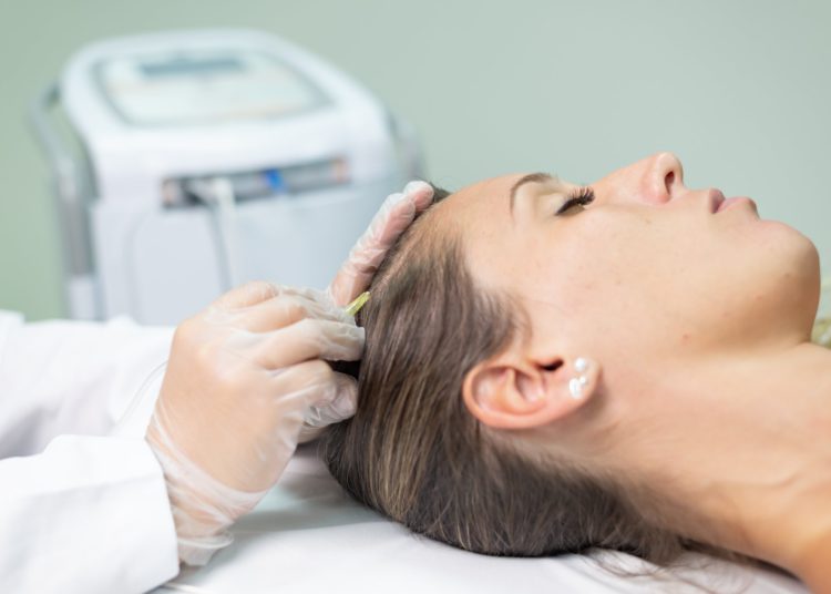 serviço de estética capilar sendo realizado, com moça deitada e outra mexendo em seu cabelo