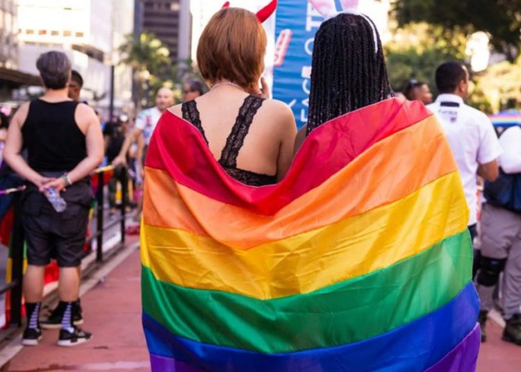 foto de mulheres enroladas por bandeira com as cores do arco íris, representando os lgbtqi+