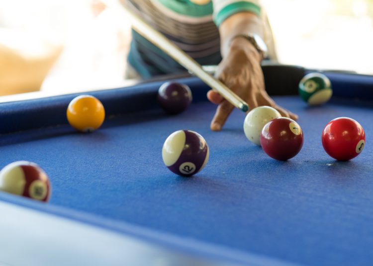 foto de mesa de sinuca, com homem posicionado para realizar jogada batendo na bola branca