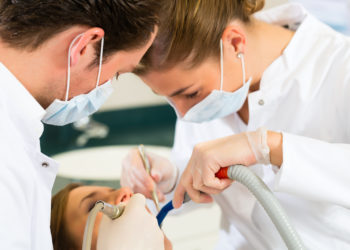 foto de tratamento dentário sendo realizado com duas pessoas ao redor de outra, que está com a boca aberta