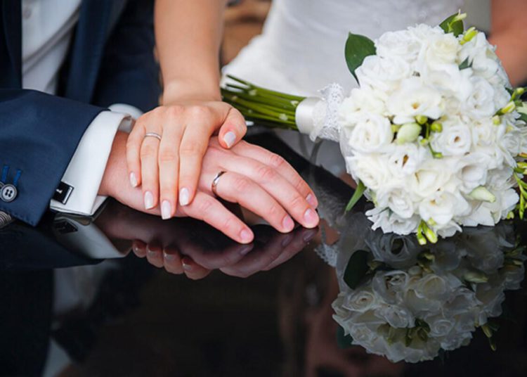 foto de casamento, com mãos vestindo aliança em foco