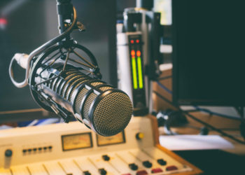 foto de estúdio de rádio, com foco no microfone e na mesa de edição