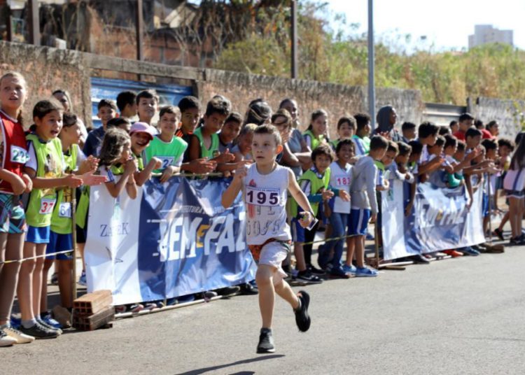 foto de criança correndo em corrida de rua, ao fundo torcida e placas de publicidade