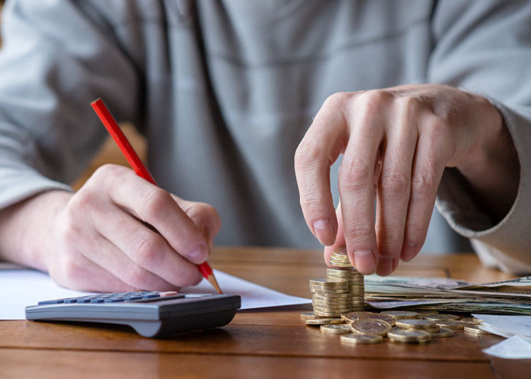 FOTO de homem mexendo em calculado e em pilha de moedas