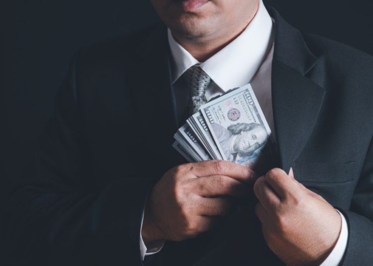 foto de pessoa de terno colocando dinheiro no paletó, em representação da corrupção