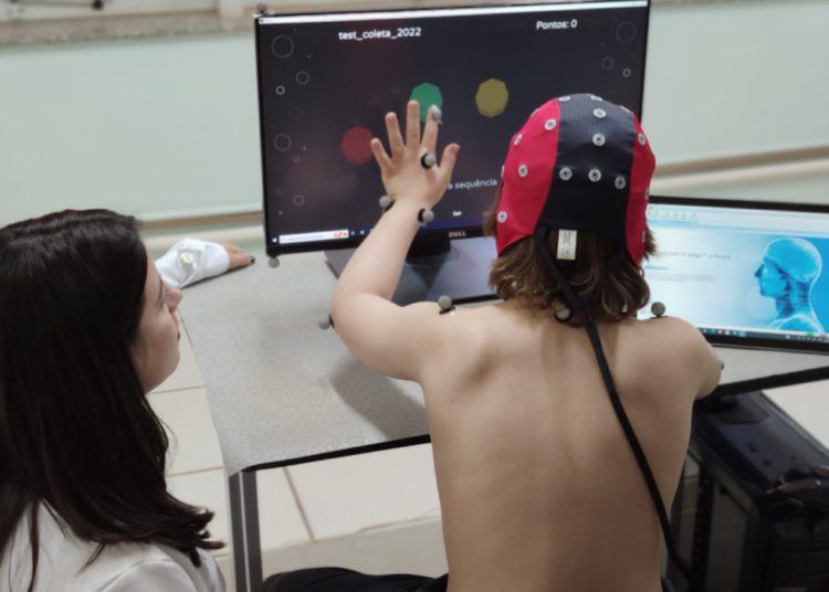 foto de criança portadora da síndrome de down realizando a gameterapia, com uma das mãos em monitor colorido