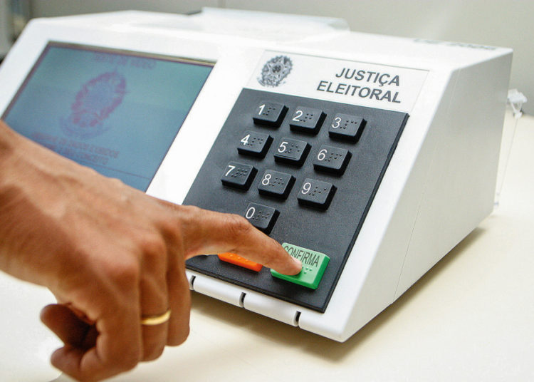 foto de urna eleitoral, com pessoa pressionando o botão de confirma