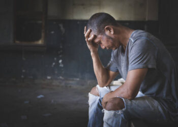 Drugs addiction and withdrawal symptoms concept. Depressed and hopeless man sitting alone after using drugs and drunk alcohol at abandoned house. International Day against Drug Abuse.